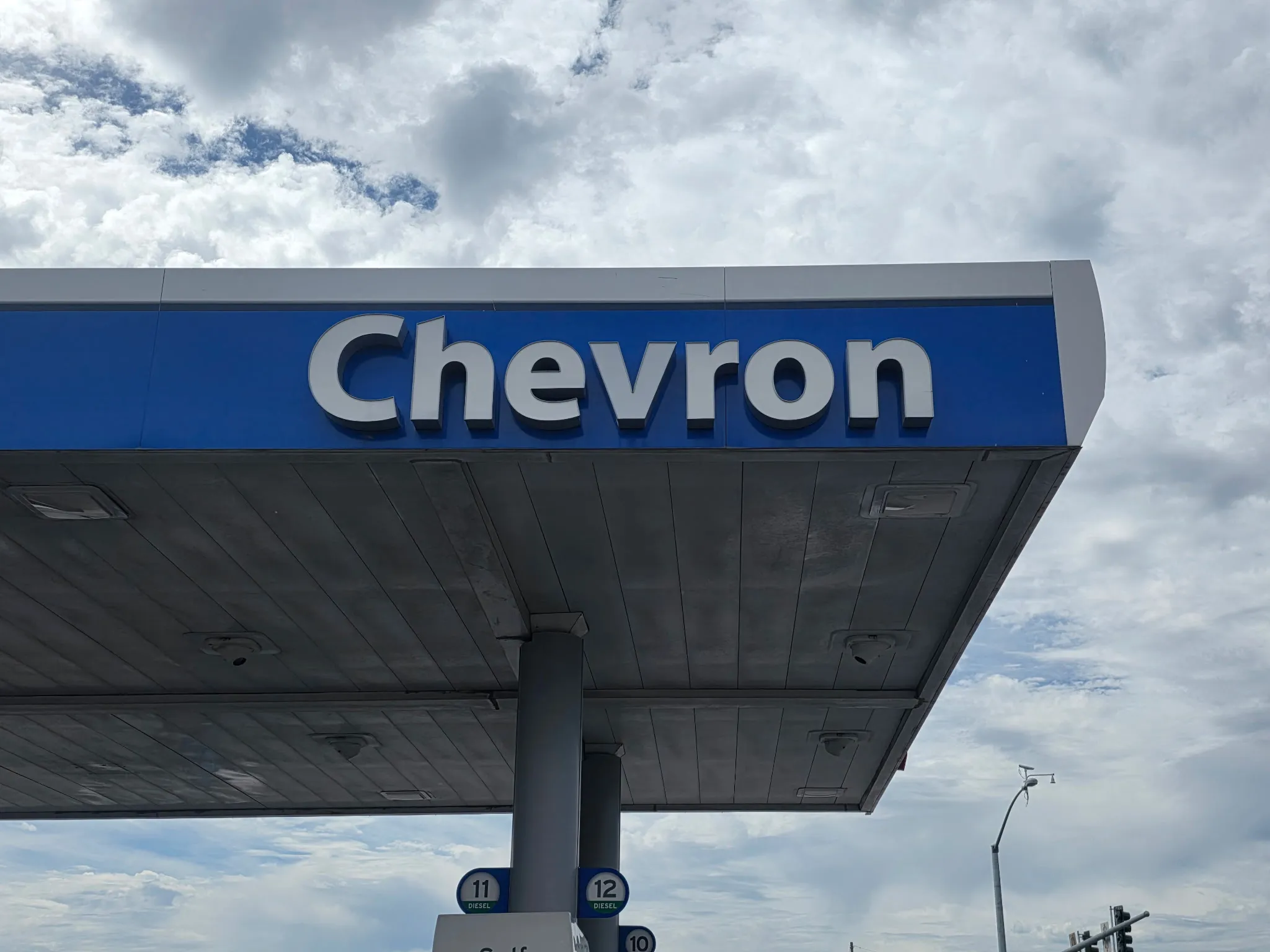 Fuel station canopy and illuminated sign photographed from below against a cloudy sky