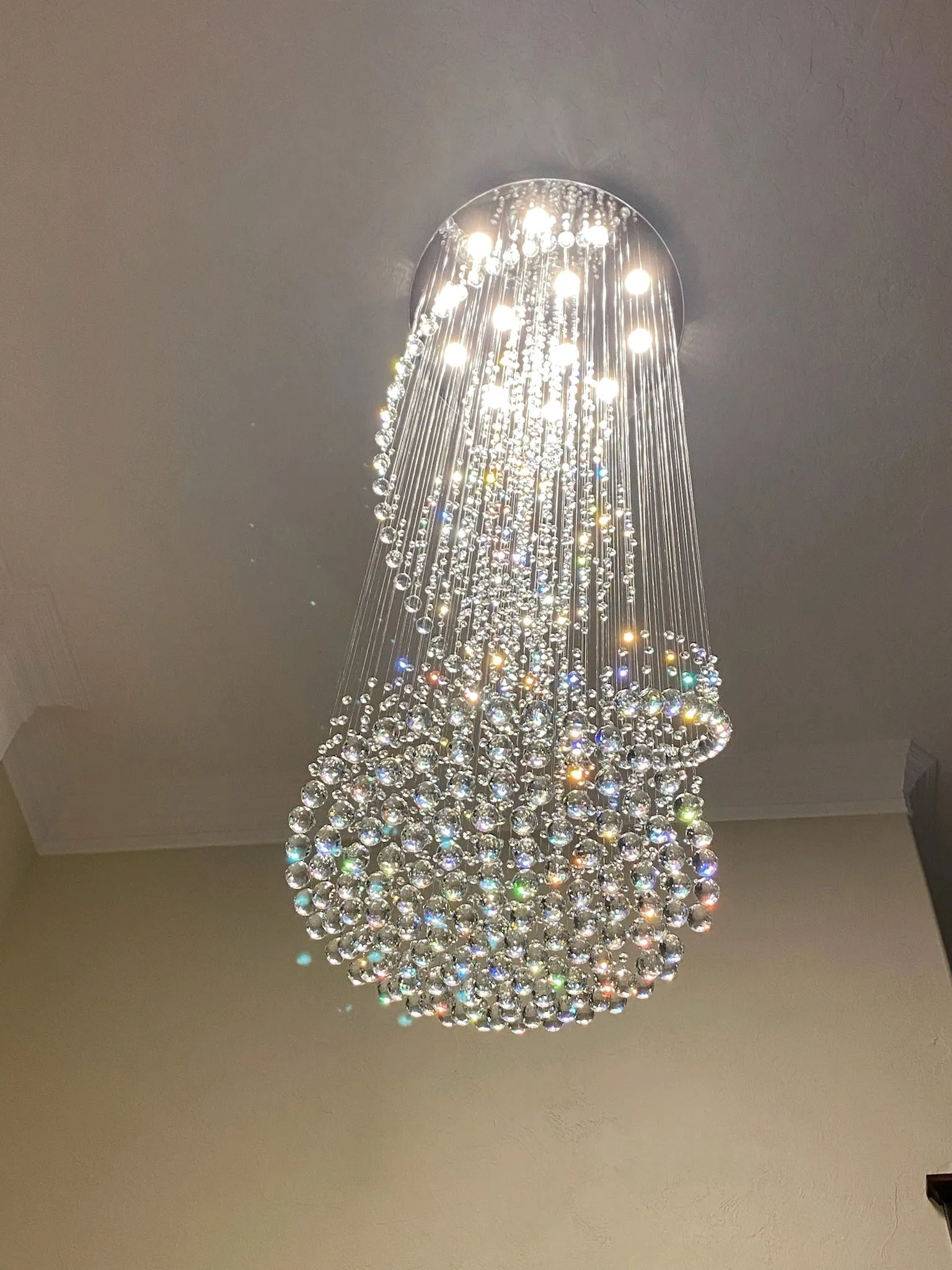 Large crystal chandelier lit, hanging close to a pale wall