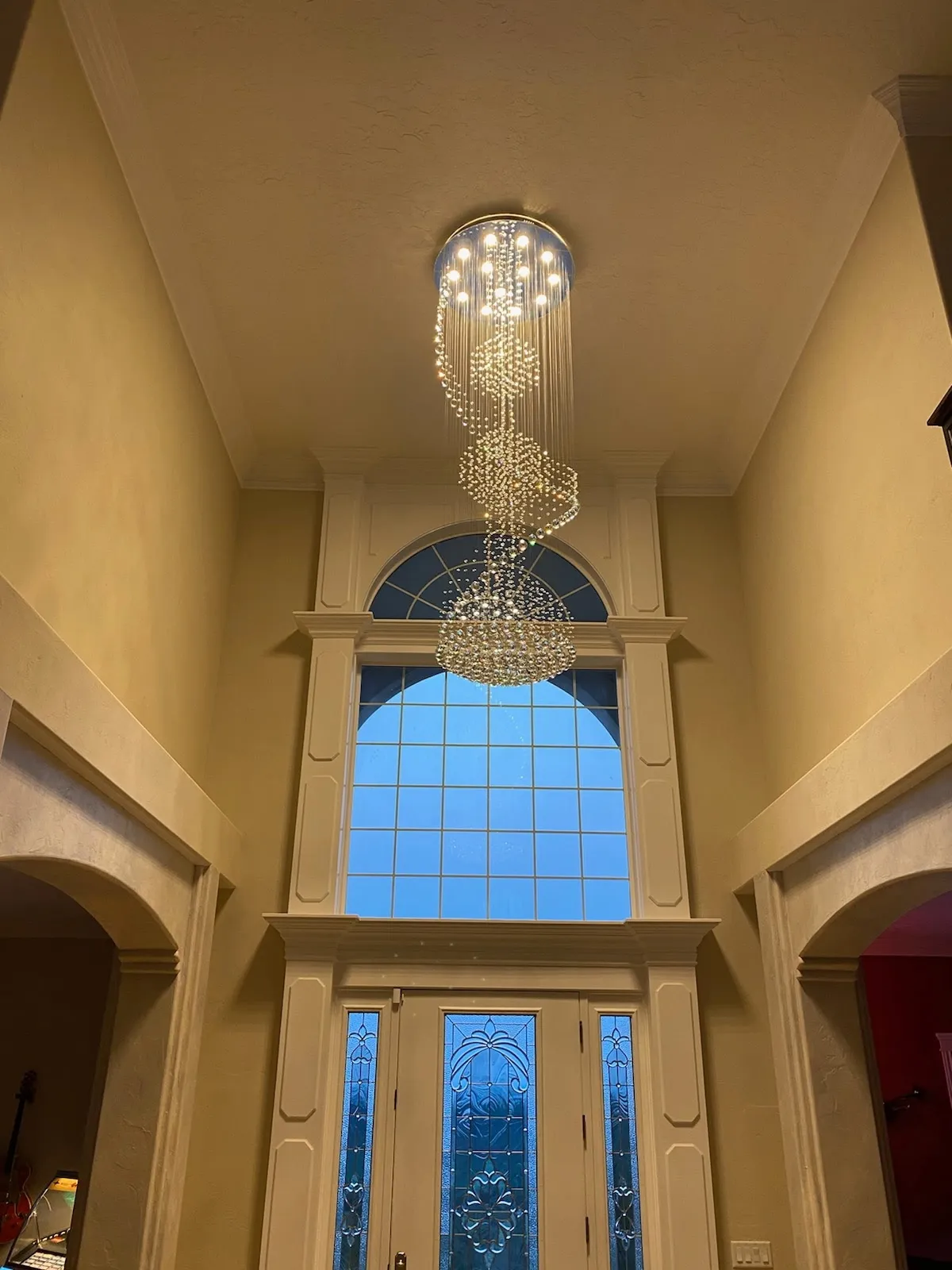 Crystal chandelier hanging in a two-storey entryway above an arched window and front door