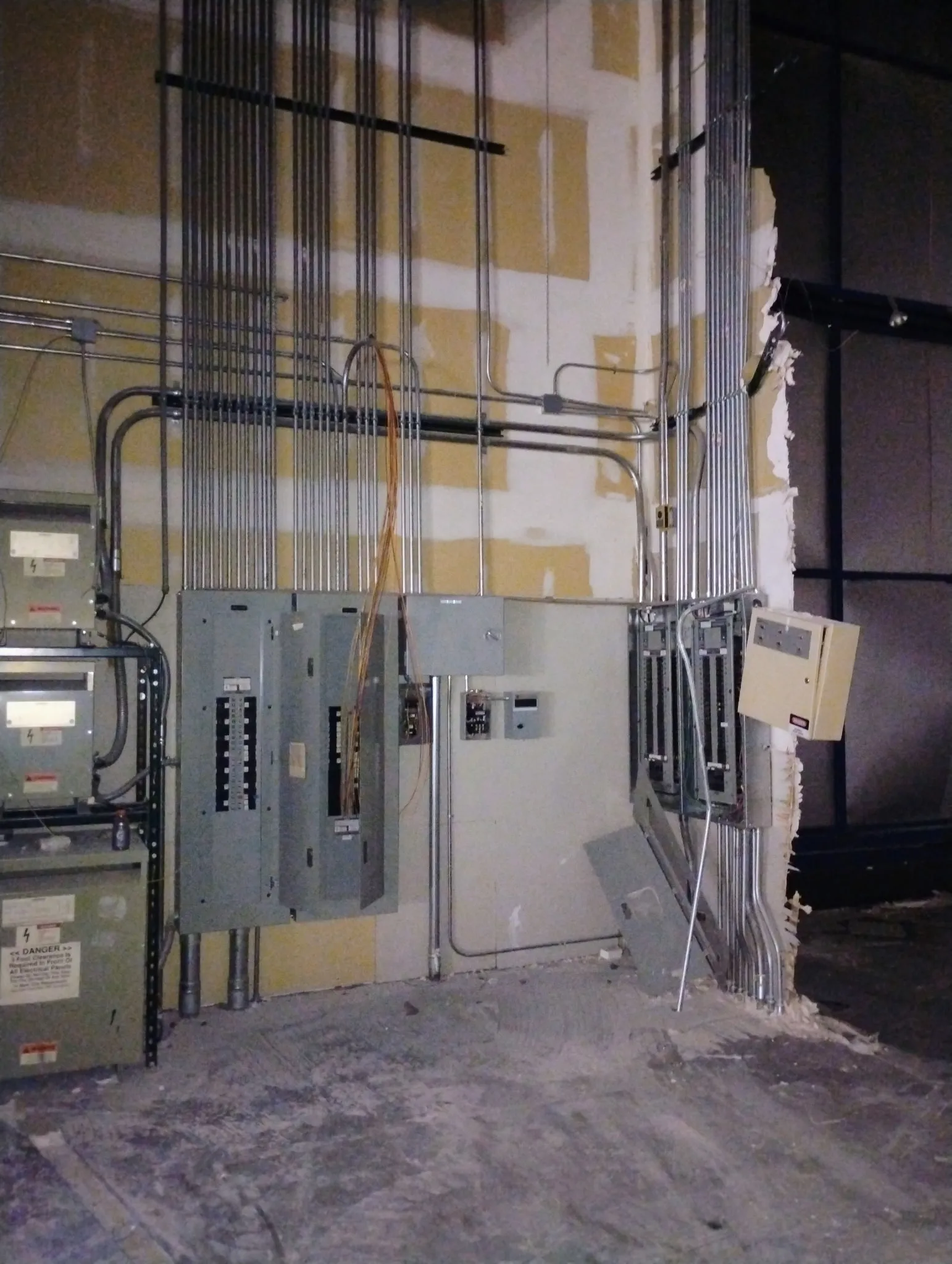 Electrical room wall with several panels, meter sockets and conduit runs feeding them