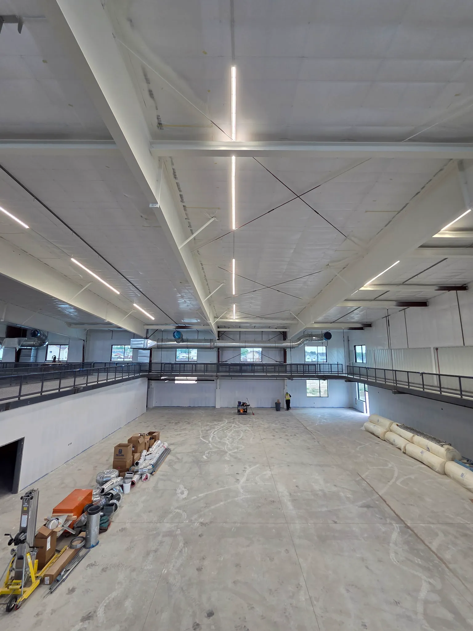 Large commercial gym interior under construction with suspended linear lighting, exposed steel framing and an elevated running track
